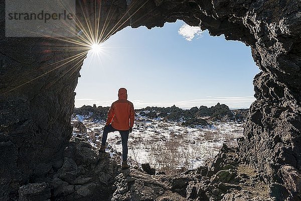 Mann in einem Felsbogen mit Sonnenstrahlen  Vulkanlandschaft  Vulkangebiet Krafla  Dimmuborgir Nationalpark  Mývatn  Island  Europa