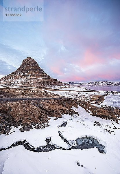 Berg Kirkjufell  Wasserfall Kirkjufellfoss zugefroren  bewölkter Himmel mit Sonnenuntergang  Grundarfjördur Fjord  Westisland  Island  Europa