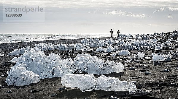 Zwei Touristen gehen am Strand spazieren  Eisschollen auf schwarzem Lavasand  Diamond Beach  Fjallsárlón Gletscherlagune  Ostisland  Island  Europa