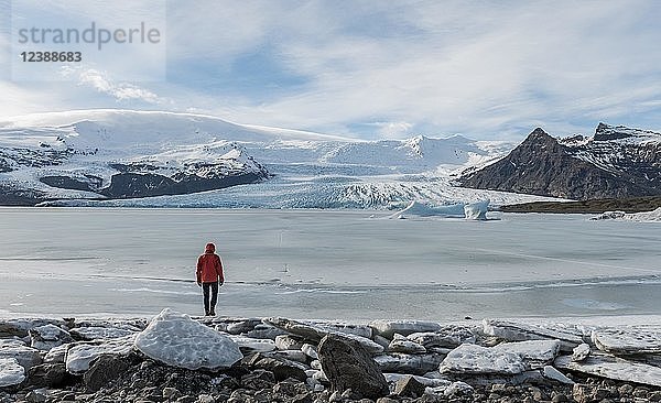 Mann steht an gefrorener Lagune mit Eisscholle  Berge  Fjallsárlón Gletscherlagune  Südisland  Island  Europa