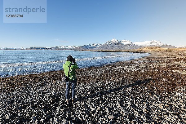Tourist beim Fotografieren an einem schwarzen Strand am Fjord Berufjörður  Austurland  Ostisland  Island  Europa