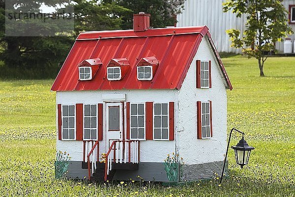 Weiße Miniaturnachbildung einer alten kanadischen Hausfassade im Landhausstil in einem Feld mit gelben Löwenzahnblüten im späten Frühling  Saint-Jean  Ile d'Orleans  Quebec  Kanada  Nordamerika