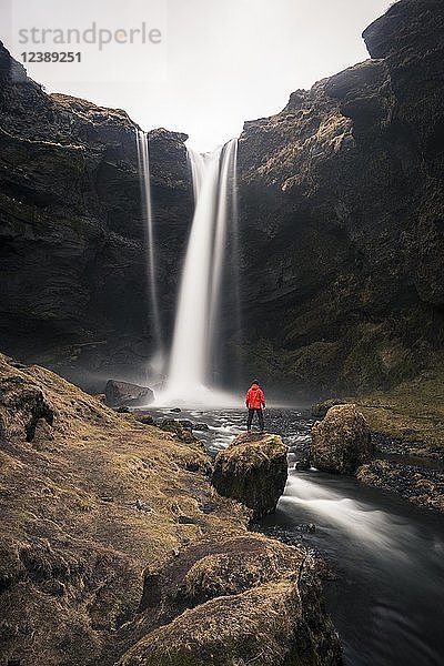 Mann in roter Jacke vor dem Wasserfall Kvernufoss in einer Schlucht  dramatische Atmosphäre  Langzeitbelichtung  bei Skógafoss  Südurland  Island  Europa