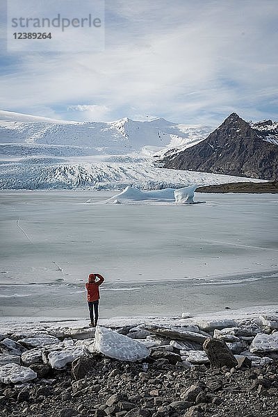 Mann steht an gefrorener Lagune mit Eisscholle  Berge  Fjallsárlón Gletscherlagune  Südisland  Island  Europa