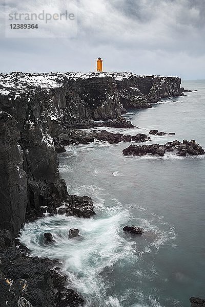 Orangefarbener Leuchtturm Öndverdarnes steht auf einer dunklen Klippe  felsige Küste  Felsvorsprünge  Langzeitbelichtung  Öndverðarnes  Westliche Region  Island  Europa