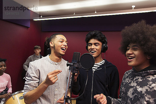 Smiling teenage boy musicians recording music  singing in sound booth