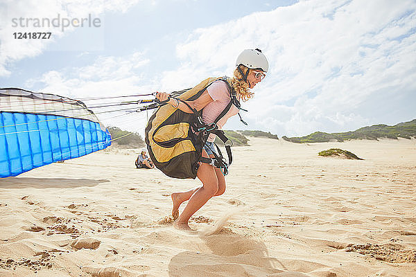 Female paraglider running with parachute on sunny beach