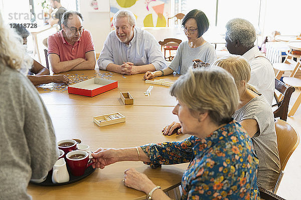 Senior friends playing games and drinking tea at table in community center