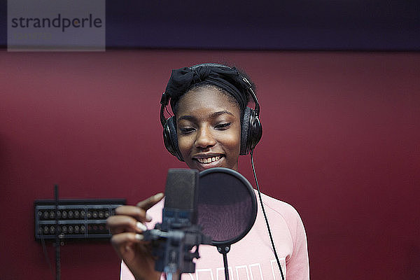 Smiling teenage girl musician recording music  singing in sound booth