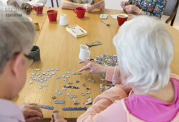 Senior friends assembling jigsaw puzzle at table in community center