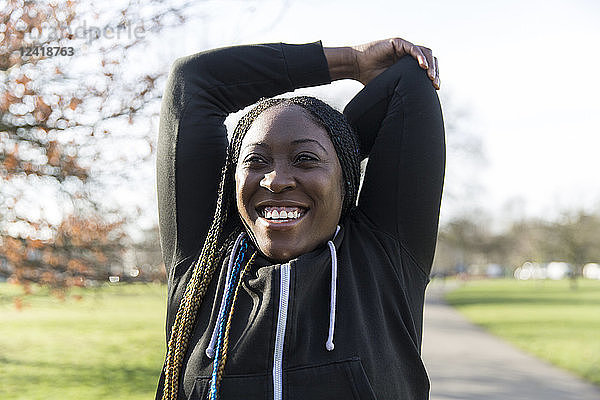 Portrait confident female runner stretching arms in park