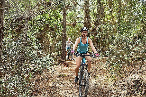 Carefree woman mountain biking on trail in woods