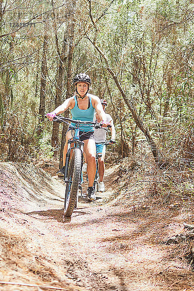 Woman mountain biking on sunny trail in woods