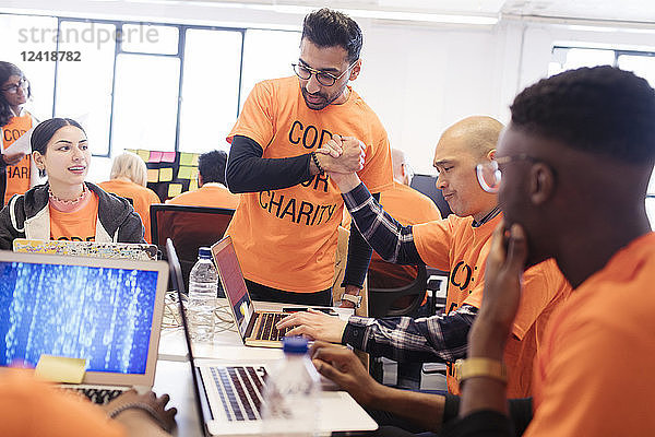 Hackers handshaking  celebrating and coding for charity at hackathon