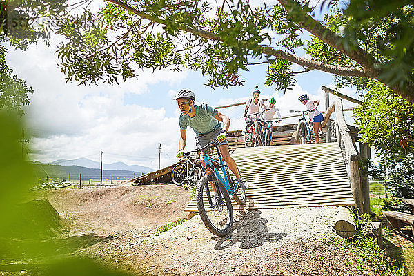 Man mountain biking down sunny obstacle course ramp