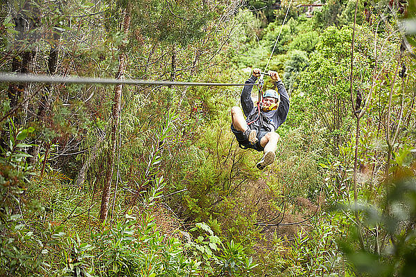 Man zip lining above trees in woods