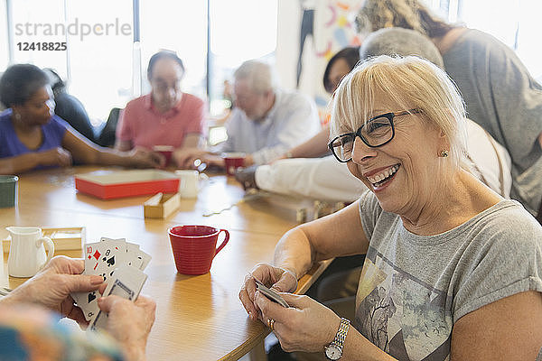 Happy senior woman playing cards with friend at table in community center