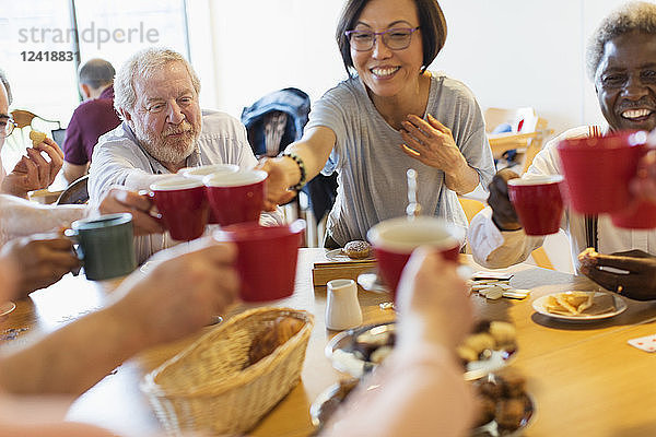 Happy senior friends enjoying afternoon tea  toasting mugs in community center