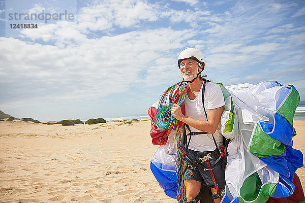 Smiling male paraglider carrying equipment and parachute on sunny beach