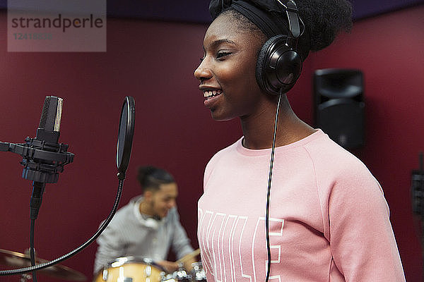 Smiling teenage girl musician recording music  singing in sound booth