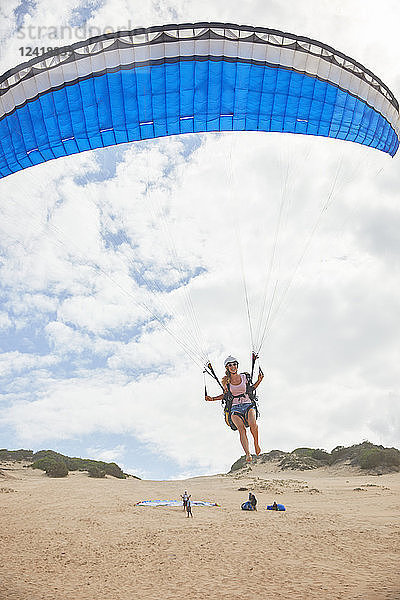 Female paraglider with parachute taking off on beach