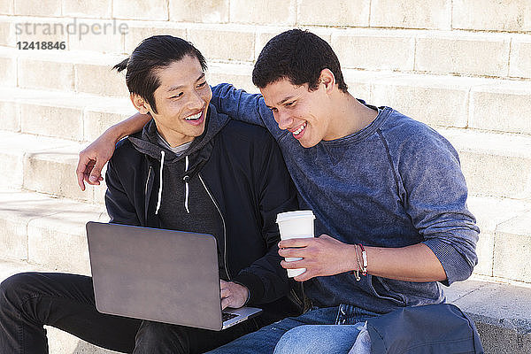 Male gay couple using laptop and drinking coffee