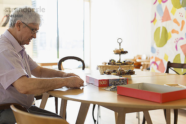 Senior man assembling jigsaw puzzle at table in community center