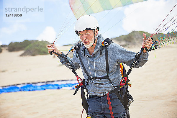 Focused mature male paraglider with equipment and parachute on beach