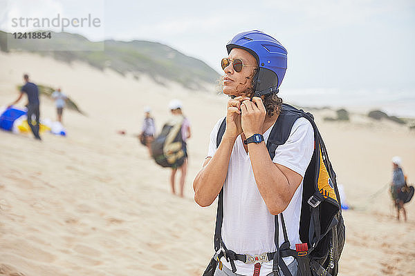 Male paraglider fastening helmet on beach
