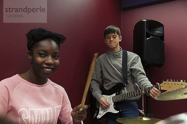 Smiling teenage musicians recording music  singing and playing electric guitar in sound booth