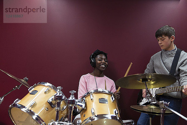 Teenage musicians recording music  playing drums and guitar in sound booth