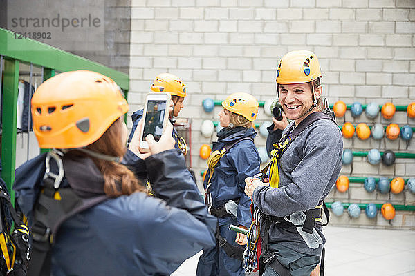 Woman with smart phone photographing man preparing zip line equipment