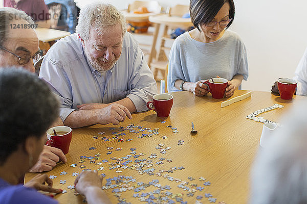 Senior friends assembling jigsaw puzzle and drinking tea at table in community center