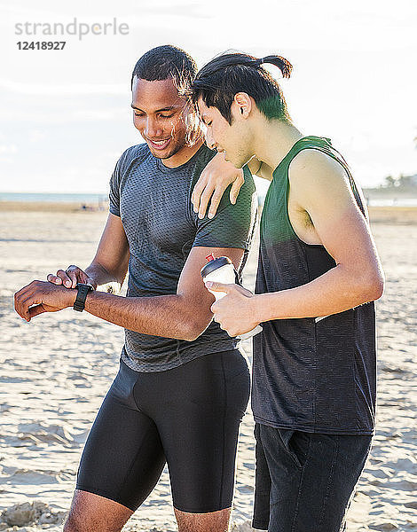 Male runners resting  checking smart watch fitness tracker on sunny beach