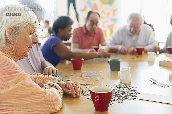 Senior woman assembling jigsaw puzzle with friends at table in community center
