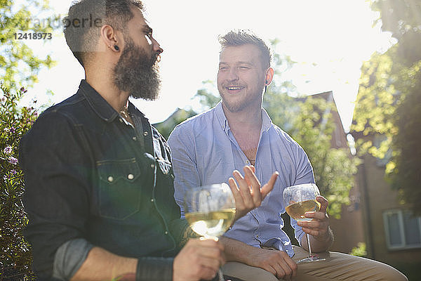 Smiling male gay couple drinking white wine in sunny garden