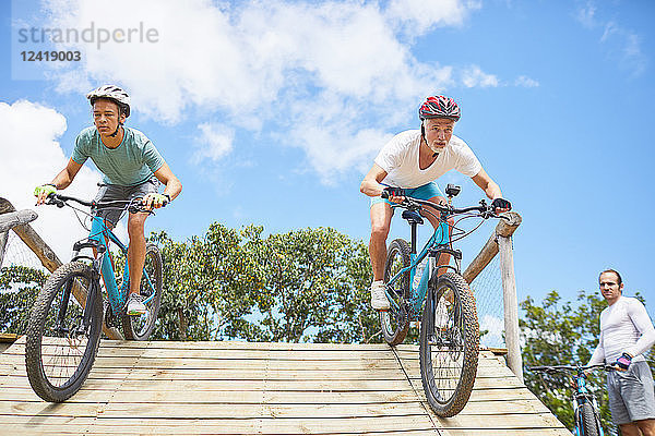 Focused men mountain biking on obstacle course ramp