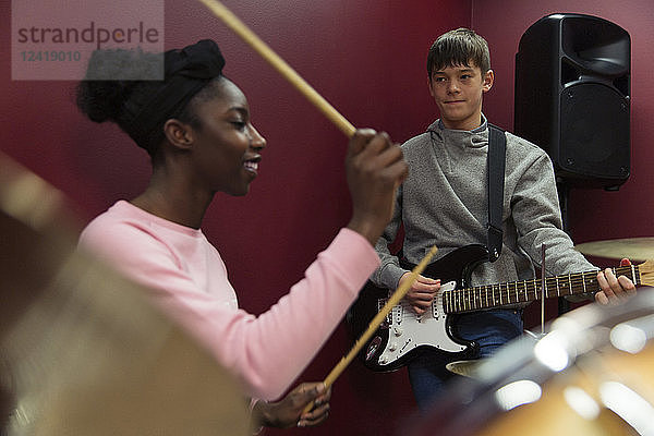 Teenage musicians recording music  playing guitar and drums in sound booth