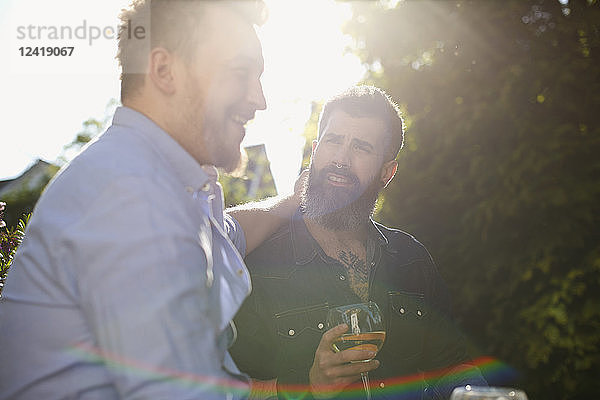 Affectionate male gay couple drinking wine in sunny garden