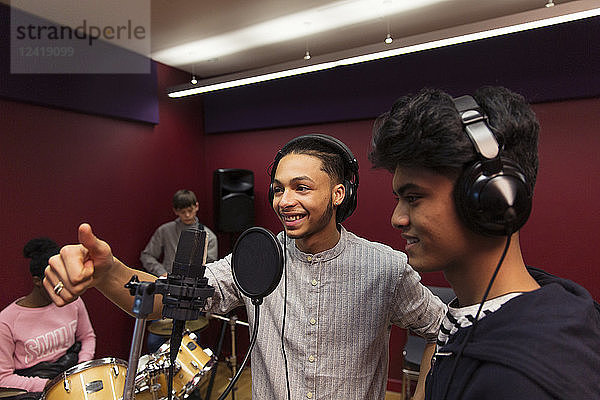 Smiling teenage musicians recording music  singing in sound booth