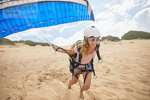 Smiling female paraglider running with parachute on beach