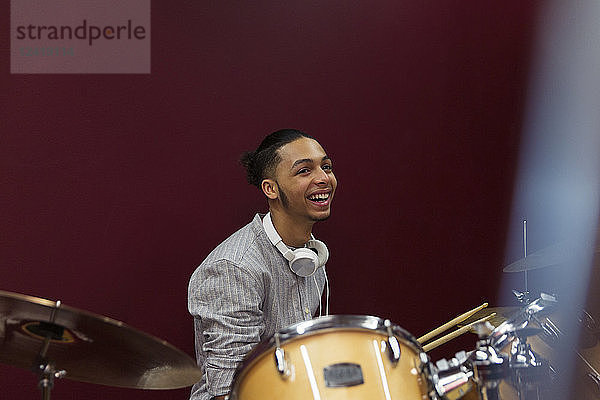 Happy teenage boy musician playing drums in sound booth