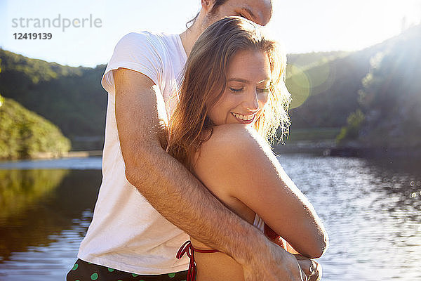 Affectionate couple hugging at sunny summer lake
