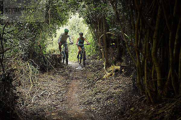 Couple mountain biking on trail in woods
