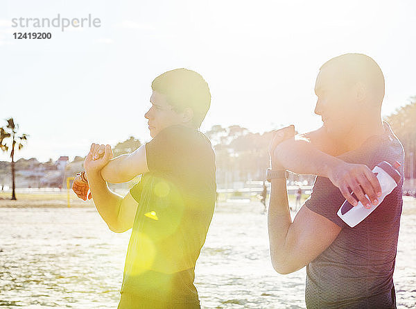 Male runners stretching arms on sunny beach