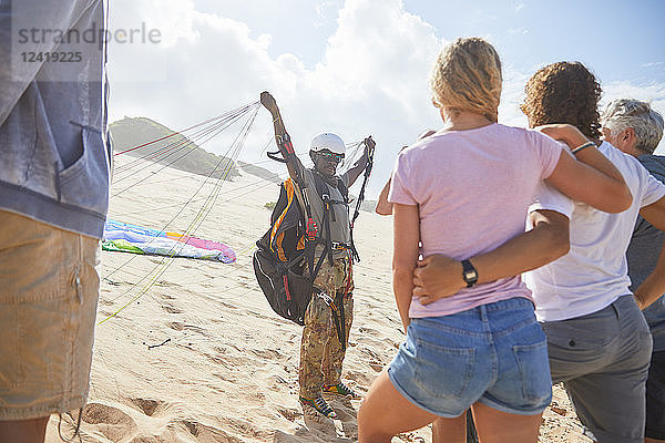 Students watching male paragliding instructor with equipment on sunny beach