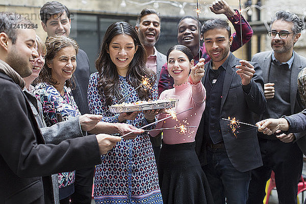 Friends with sparklers celebrating with woman holding birthday cake
