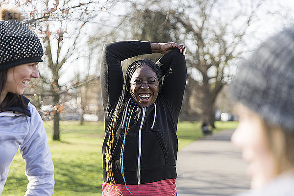Smiling female runner stretching in sunny park