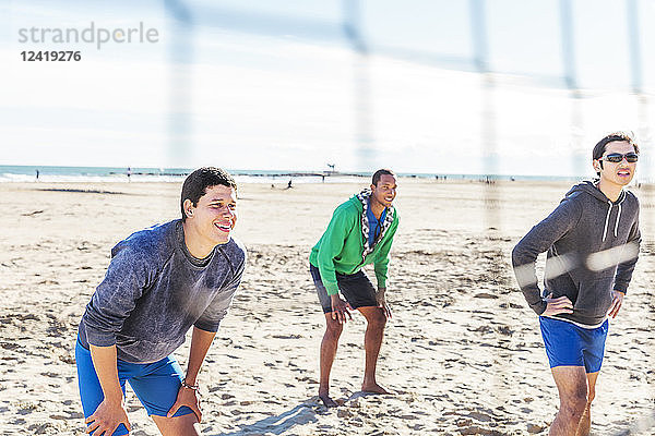 Men playing beach volleyball on sunny beach