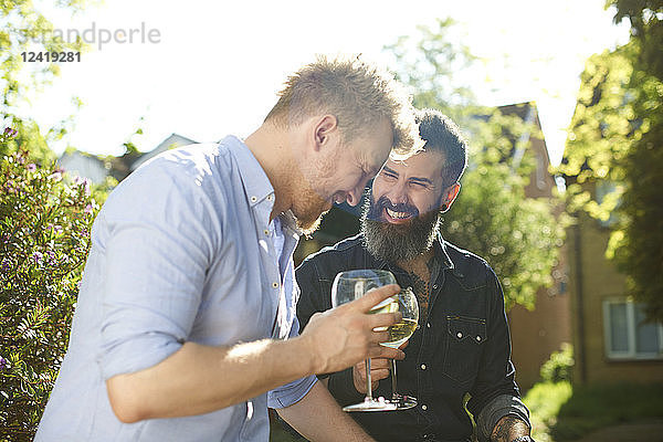 Happy male gay couple drinking wine in sunny garden